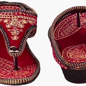 May include: Pair of red and gold embroidered sandals. The sandals feature intricate gold embroidery on a red background, with a black and gold braided trim. The design includes a toe post and a small heel.