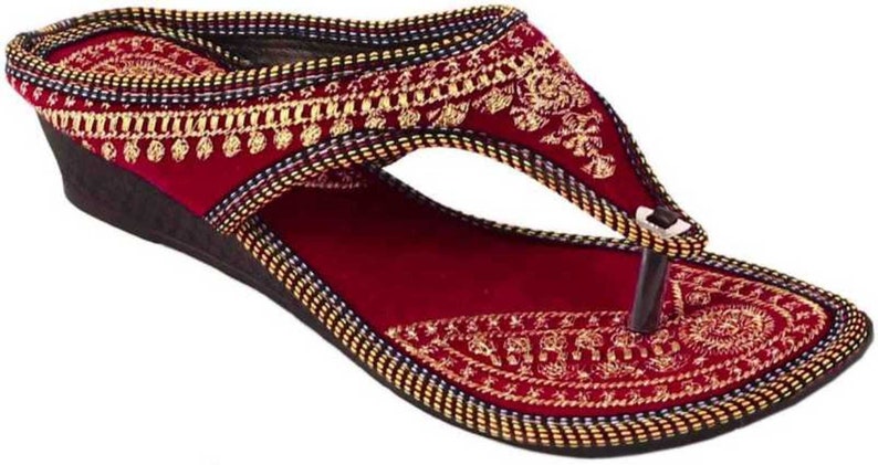 May include: Burgundy wedge sandal with intricate gold embroidery. The sandal features a thong-style design with a dark brown sole and a decorative pattern around the edges. A stylish footwear option.