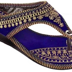 May include: A blue sandal with a wedge heel. The sandal features intricate gold embroidery along the edges and straps, with a decorative pattern on the footbed. The thong strap is white and the sole is black.