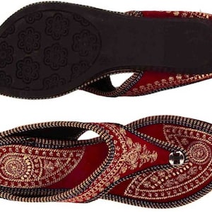 May include: Burgundy and gold embroidered sandals. The sandals feature intricate gold threadwork on a burgundy base, with a black sole. The design includes a toe loop and a decorative button. The sole has a floral pattern.