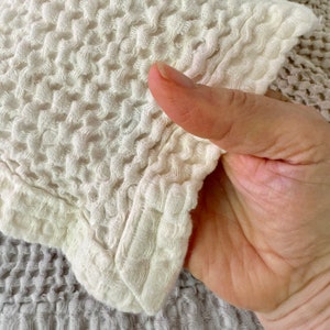 May include: A close-up of a white waffle weave fabric. The fabric is textured and has a soft, fluffy appearance.