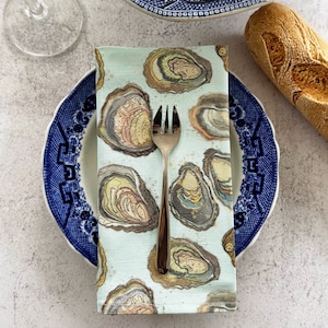 May include: A blue and white oyster-themed napkin with a silver fork on top. The napkin is folded in half and is sitting on a blue and white plate.