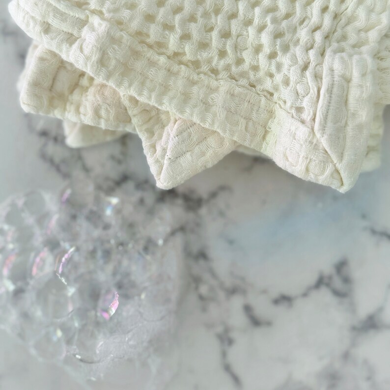 May include: A white waffle weave cotton towel folded on a white marble surface.