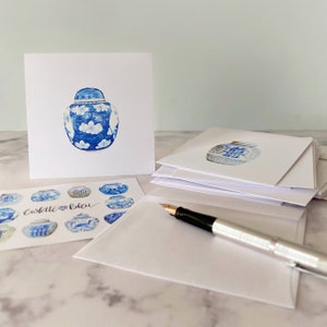 May include: A stack of blank white note cards with a blue and white porcelain ginger jar illustration on the top card. The text "Coslette Bleu" is printed on a card with a pattern of blue and white ginger jars.