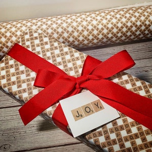 May include: A gift wrapped in brown paper with a white and brown checkered pattern. The paper is decorated with the word "JOYO" in black letters. A red ribbon is tied around the package with a bow on top.