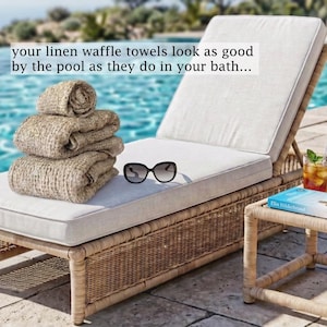May include: A stack of three beige linen waffle towels, black sunglasses, and a book on a light-colored chaise lounge. The text reads: your linen waffle towels look as good by the pool as they do in your bath...