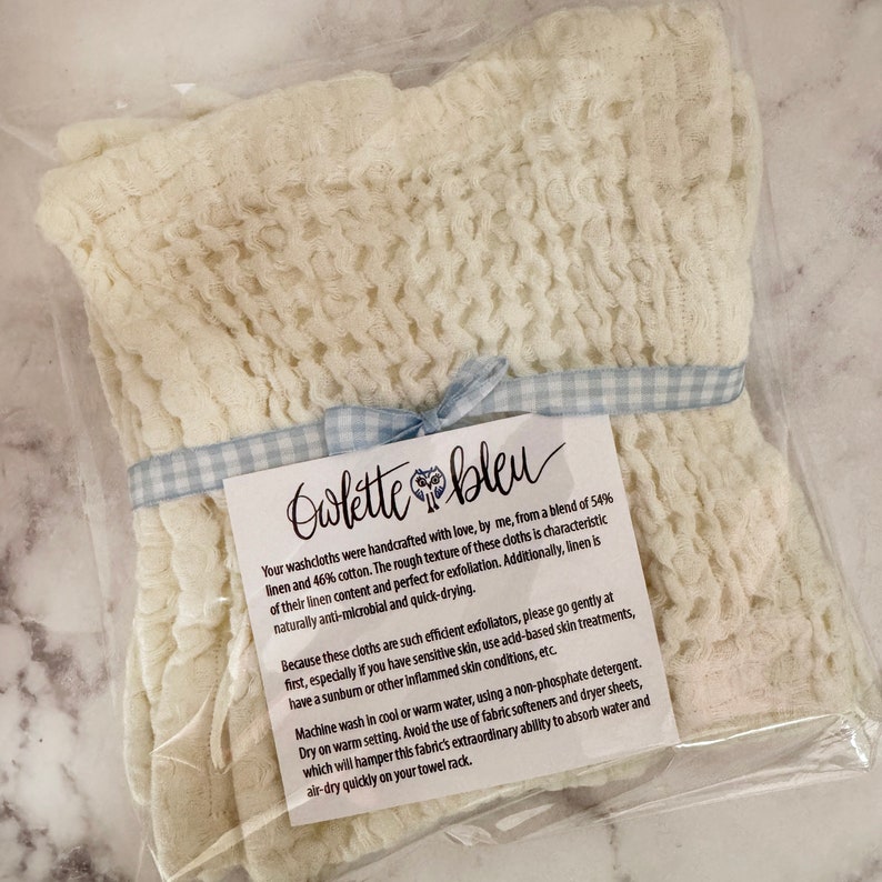 May include: A white washcloth with a blue and white checkered ribbon tied around it. The washcloth is packaged in a clear plastic bag with a white card that reads "Owlette bleu" and includes instructions for washing and drying the washcloth.