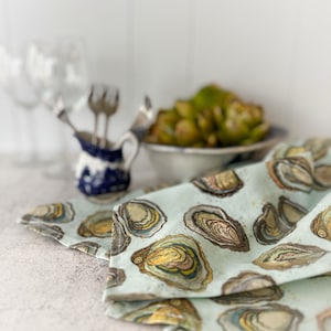 May include: A light blue tea towel with a pattern of oyster shells in shades of brown, yellow, and green.