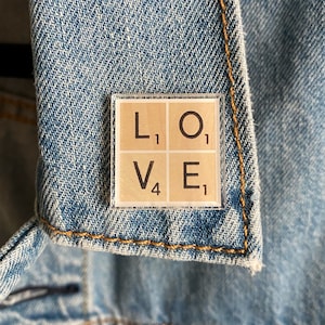 May include: A close-up of a brown and white tile with the letters "LOVE" spelled out. Each letter is on a separate tile and has a subscript number next to it. The tiles are framed in a clear plastic frame.
