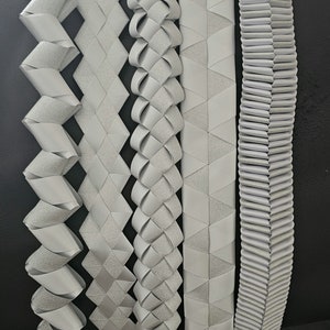 May include: Six different styles of silver ribbon trim, each with a unique pattern and texture. The ribbon is arranged vertically, with the leftmost ribbon having a zig-zag pattern and the rightmost ribbon having a pleated pattern.