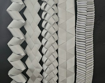 May include: Six different styles of silver ribbon trim, each with a unique pattern and texture. The ribbon is arranged vertically, with the leftmost ribbon having a zig-zag pattern and the rightmost ribbon having a pleated pattern.