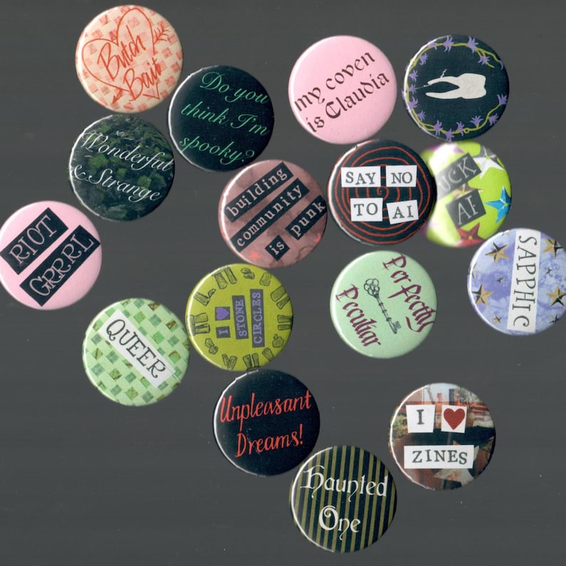 Pu&ograve; includere: Una collezione di bottoni rotondi con vari disegni e testo. I bottoni presentano frasi come "Butch Bait", "Queer" e "Unpleasant Dreams!". I colori includono rosa, verde, nero e bianco. Alcuni bottoni hanno sfondi a motivi.