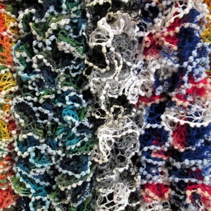 May include: A close-up of a multi-coloured crocheted scarf with a ruffled texture. The scarf is made of yarn in shades of red, blue, green, white, and orange.