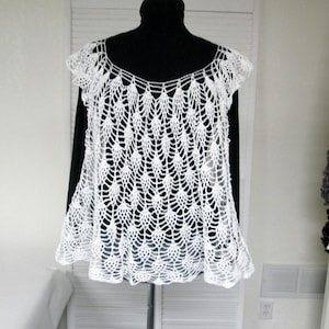 May include: White crocheted top with a scalloped design. The top has a scoop neck and short sleeves.