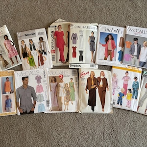 Könnte beinhalten: Eine Sammlung von 12 Schnittmustern für verschiedene Kleidungsstücke. Die Schnittmuster stammen von verschiedenen Marken, darunter Threads, Butterick, McCall's, Simplicity und Wloor. Die Schnittmuster bieten eine Vielzahl von Stilen, darunter Kleider, Hemden, Hosen und Röcke.
