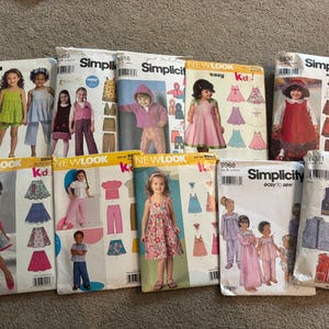 May include: A collection of nine sewing pattern envelopes for children's clothing, featuring various designs including dresses, skirts, pants, vests, and tops. The envelopes are branded as Simplicity and New Look, displaying illustrations of children wearing the finished garments.