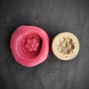 Puede incluir: Un molde de silicona rojo con un diseño floral detallado y un molde de metal dorado con un diseño similar.