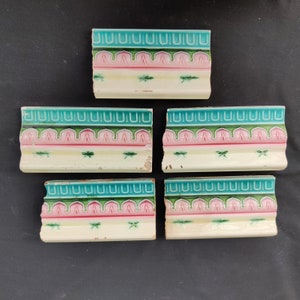 May include: Five antique ceramic tile trim pieces with a repeating pattern of green, pink, and white. The tiles have a floral design with dragonfly accents.