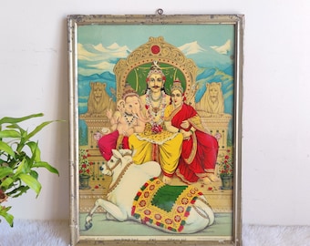 May include: A framed vintage print of a Hindu deity, Shiva, with his wife Parvati and son Ganesha. The print is in a silver frame and features a colourful depiction of the deities sitting on a throne with a white bull.