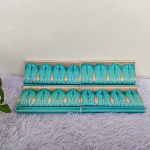 May include: Four turquoise and cream ceramic tiles with a decorative pattern of stylized teardrop shapes. The tiles are arranged in a row and have a slightly curved shape.