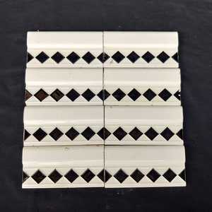 May include: Eight white ceramic tiles with black diamond patterns. The tiles have a raised edge and are arranged in two rows of four.