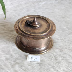 May include: A vintage, bronze-colored metal container with a lid and a small handle. The container has a round base and a slightly domed lid with a conical knob. The label reads "IP 64".