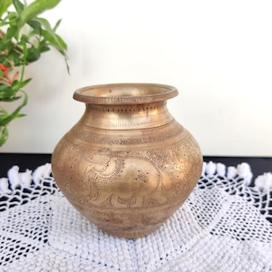 May include: A small, antique brass vase with intricate etched designs of elephants and floral patterns. The vase has a rounded body and a slightly flared lip.