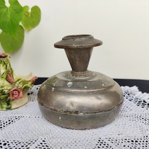 Puede incluir: Un jarrón de metal plateado con base redonda y parte superior acampanada. El jarrón tiene un diseño decorativo alrededor del borde superior.