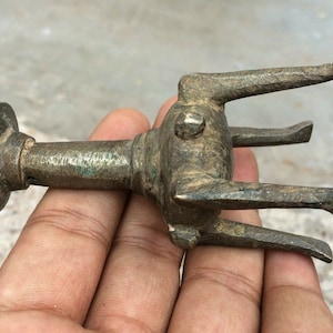 May include: A small, antique, bronze-colored metal object with a round base and three prongs. The object has a textured surface and appears to be a decorative piece.