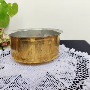 May include: A round, brass bowl with a silver interior. The bowl is sitting on a white crocheted doily.
