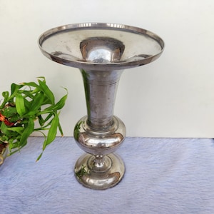 Puede incluir: Un jarrón de plata con una abertura ancha y acampanada y una base redonda. El jarrón tiene un acabado liso y pulido.