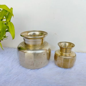 May include: Two silver metal containers, one larger than the other, with a rounded shape and a slightly flared top. The containers are sitting on a white fluffy surface.