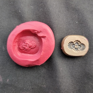 Puede incluir: Un molde de silicona rojo con un diseño floral y un sello de latón con un diseño similar.