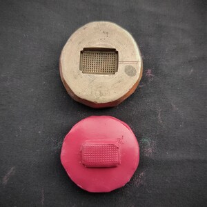 Puede incluir: Dos moldes redondos y planos para hacer joyas. El molde superior está hecho de metal y tiene un recorte rectangular. El molde inferior está hecho de goma rosa y tiene un recorte rectangular.