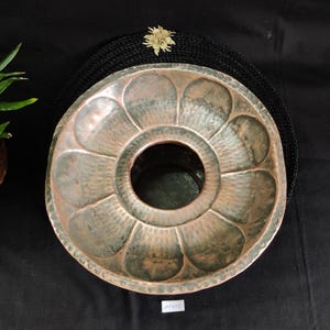 Puede incluir: Una maceta de cobre con un diseño decorativo. La maceta tiene una abertura circular en el centro y un borde festoneado.