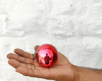 Puede incluir: Un adorno de Navidad de vidrio rojo con una superficie reflectante. El adorno se está sosteniendo en la mano de una persona.