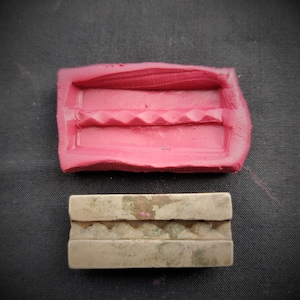 Puede incluir: Un molde de silicona rosa con un diseño texturizado, y una barra de metal plateada con un diseño texturizado similar.