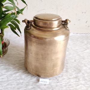Peut inclure: Un récipient en laiton vintage avec un couvercle et deux poignées. Le récipient a une forme cylindrique avec des lignes gravées horizontales et une base légèrement arrondie. Le couvercle est bien ajusté. Le récipient est de couleur dorée chaude.