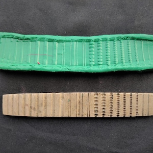 Puede incluir: Un molde de goma verde y un sello de metal plateado con un patrón repetitivo de líneas y puntos.