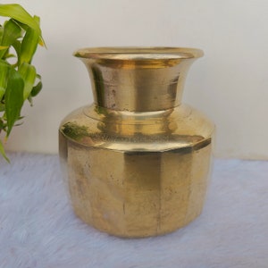 May include: A gold-colored brass vase with a rounded body and a flared top. The vase has a faceted design and a smooth, polished finish.