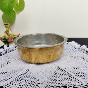 May include: A round brass bowl with a hammered finish and a silver lining. The bowl is sitting on a white crocheted doily.