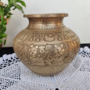 May include: A brass vase with intricate etched designs of people and geometric patterns. The vase has a rounded body and a wide mouth.