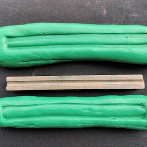 Puede incluir: Dos piezas rectangulares de arcilla verde con un diseño acanalado y una barra de metal plateada en el medio.