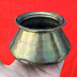 May include: A small, brass pot with a rounded bottom and a flared rim. The pot has a greenish patina and appears to be antique.