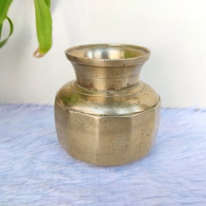 May include: A small, octagonal brass vase with a wide mouth and a slightly flared rim. The vase has a worn, antique finish and is likely of Indian origin.