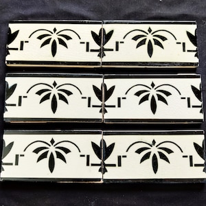 May include: Three black and white ceramic tiles with a repeating pattern of stylized black floral designs on a white background. The tiles have a black border.