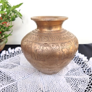 May include: A brass vase with intricate carvings of figures and patterns. The vase has a rounded body and a wide mouth.