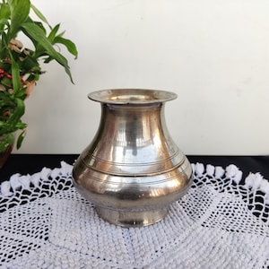 May include: A silver metal vase with a wide mouth and a rounded body. The vase has a smooth, shiny finish and a slightly flared lip.