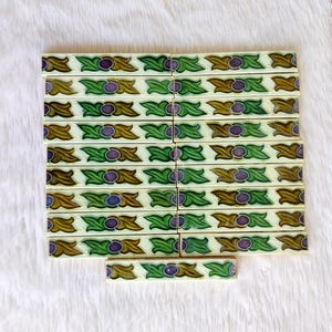 May include: A set of 15 vintage ceramic tiles with a repeating pattern of green leaves, brown swirls, and purple circles. The tiles are arranged in rows and are ready to be used for a decorative project.