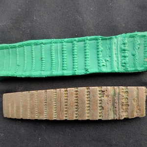 Puede incluir: Un molde de goma verde y un sello de metal bronce con un patrón repetitivo de pequeños círculos.